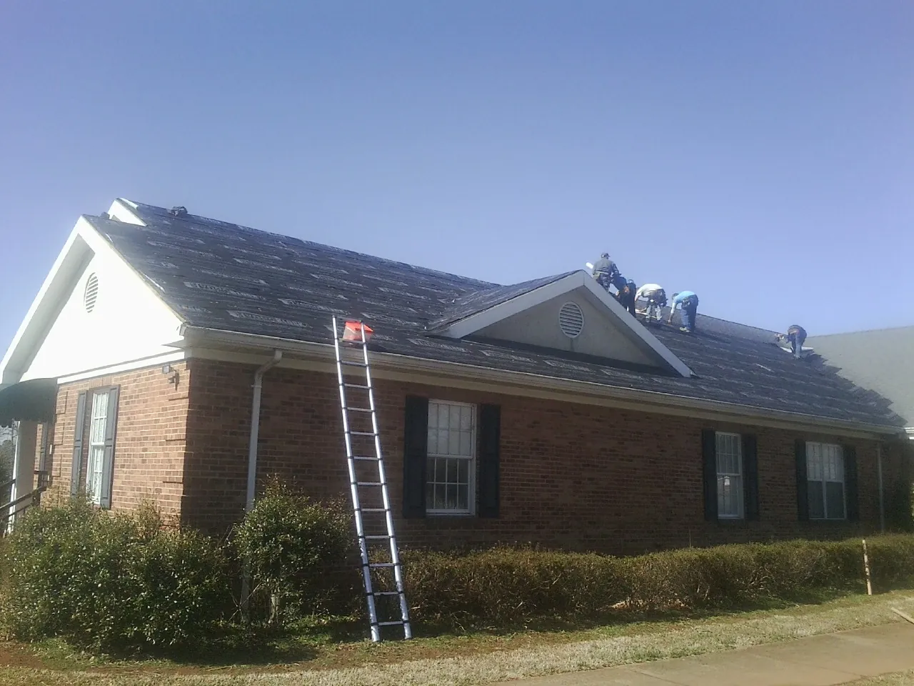 Crew tearing shingles off a brick ranch roof with a ladder set — Emergency Roof Repair work by our crew in Dennis Port