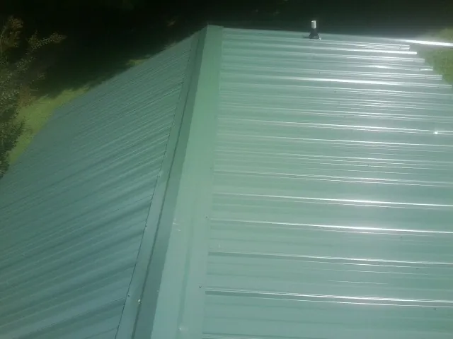 New green metal panels meeting at the ridge of a roof — Flat Roof Repair work by our crew in Dennis Port