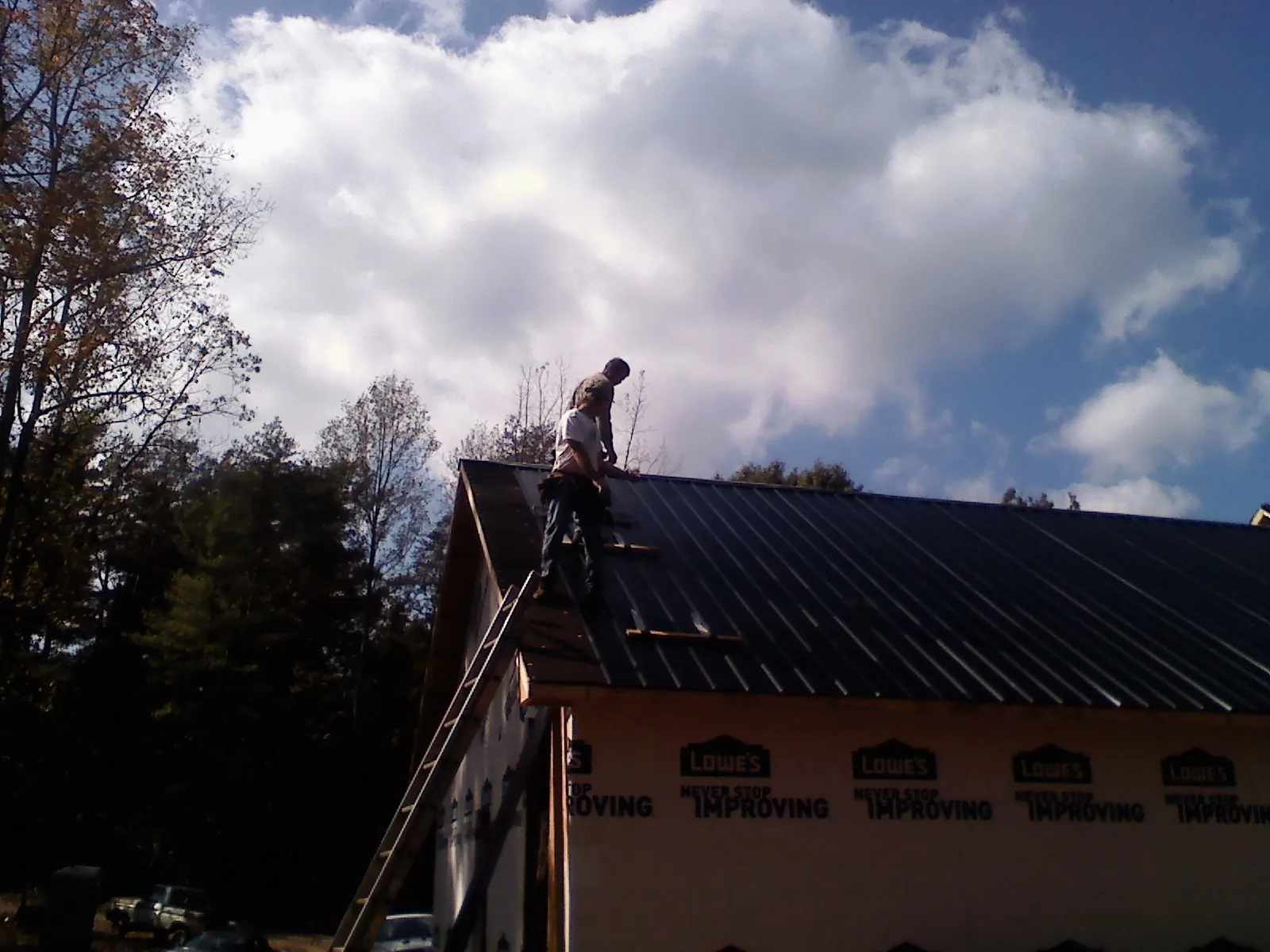 Roofer fastening dark metal panels high against a cloudy sky, from a Roof Inspection job in Dennis Port