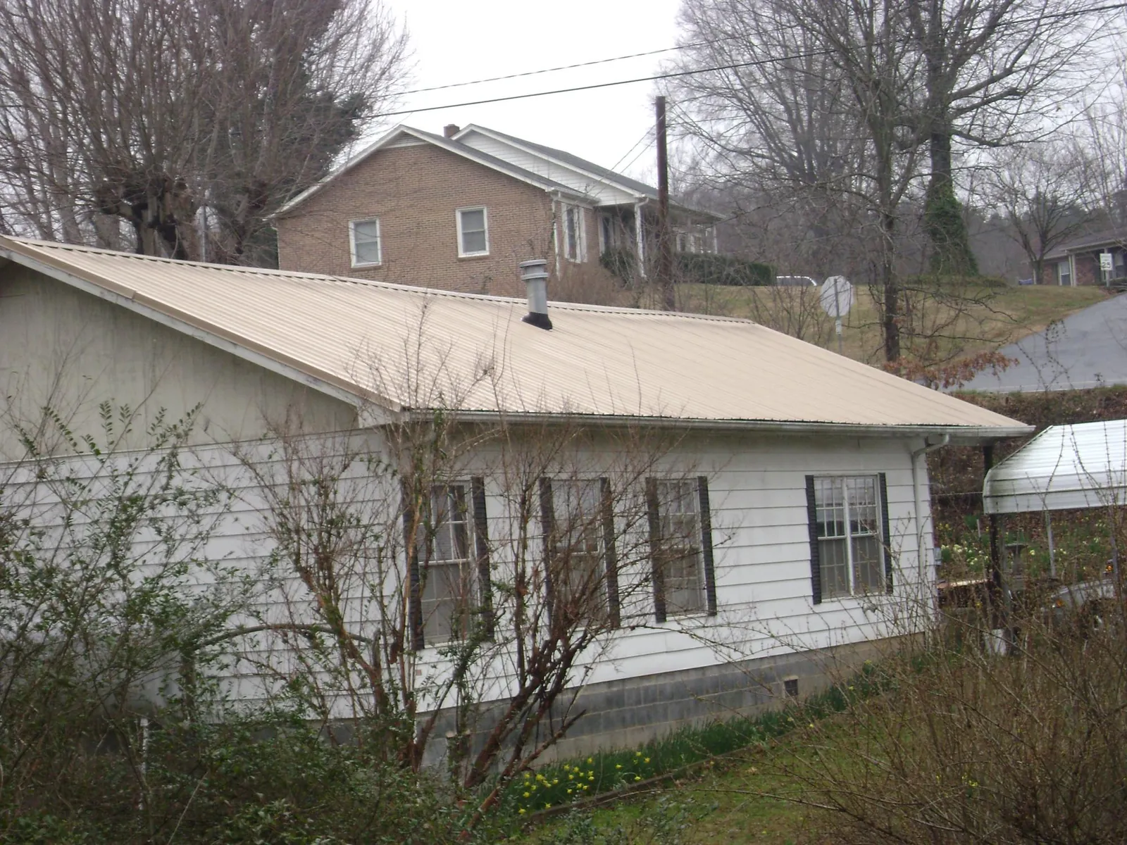 Tan metal roof on a white sided house set into a hillside — Commercial Roofing by Roofing Brothers in Dennis Port