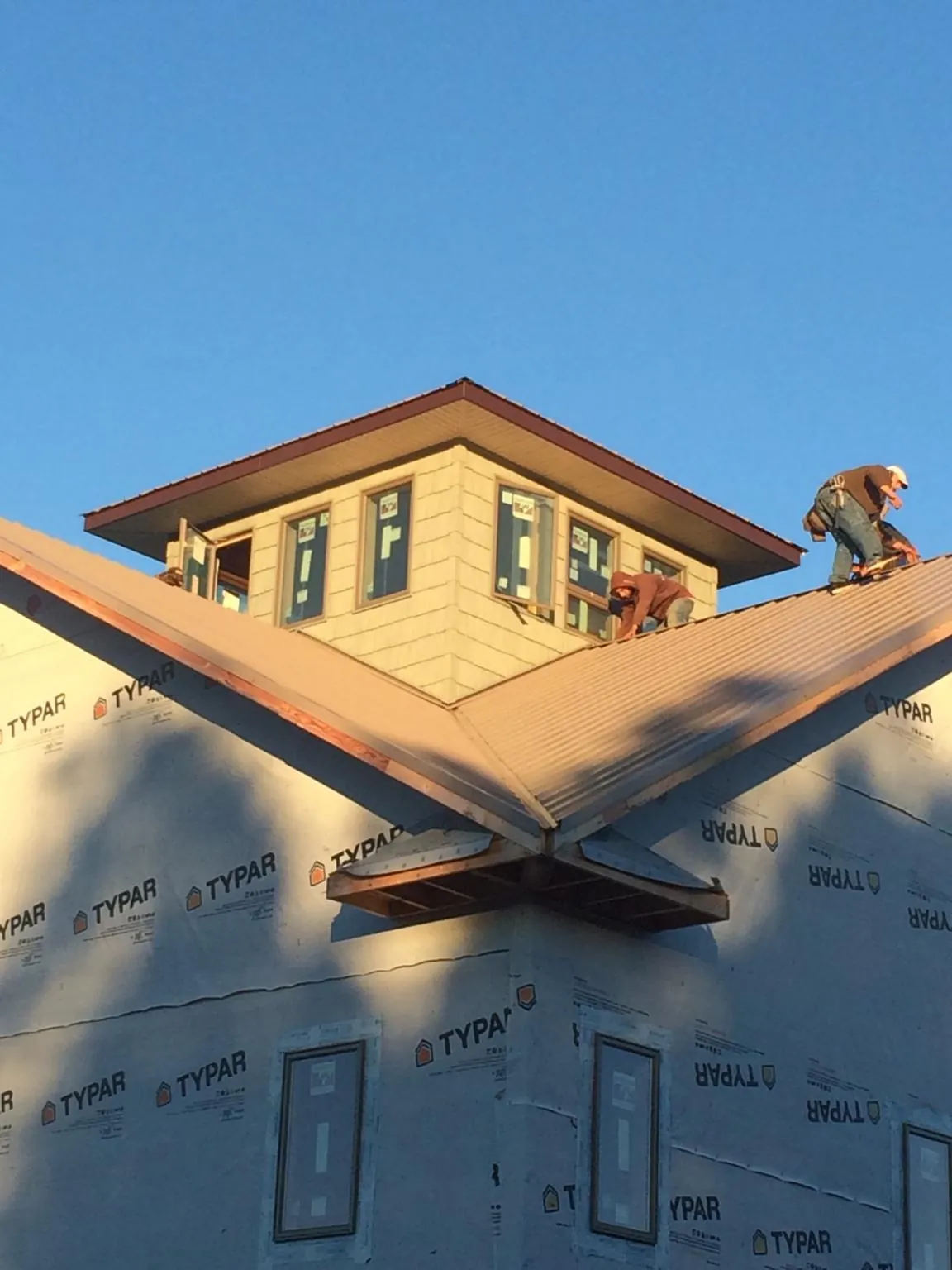 Roofers working around a rooftop cupola on a new metal roof at sunset — Roof Waterproofing in Dennis Port by Roofing Brothers